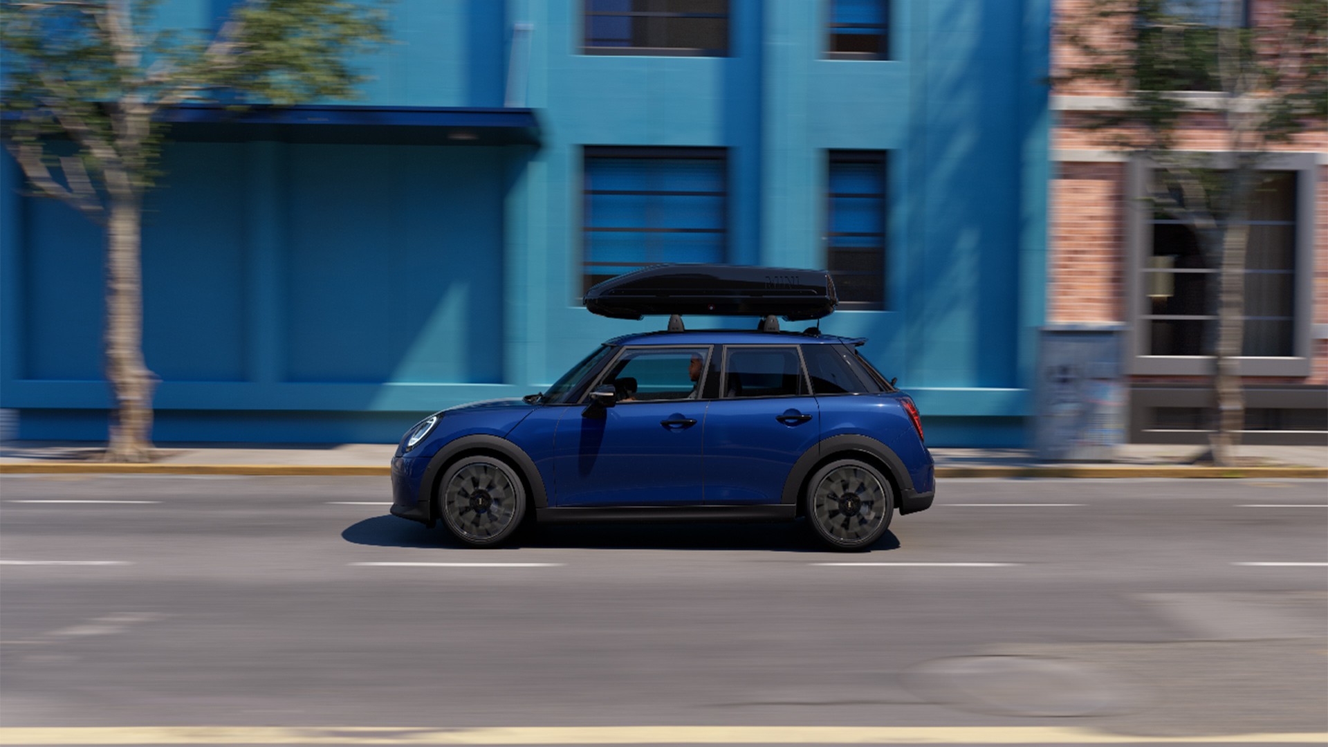 Three quarter front view of MINI Aceman in Indigo Sunset Blue equipped with MINI Roof Rack, carrying a MINI Roof Box 320. 